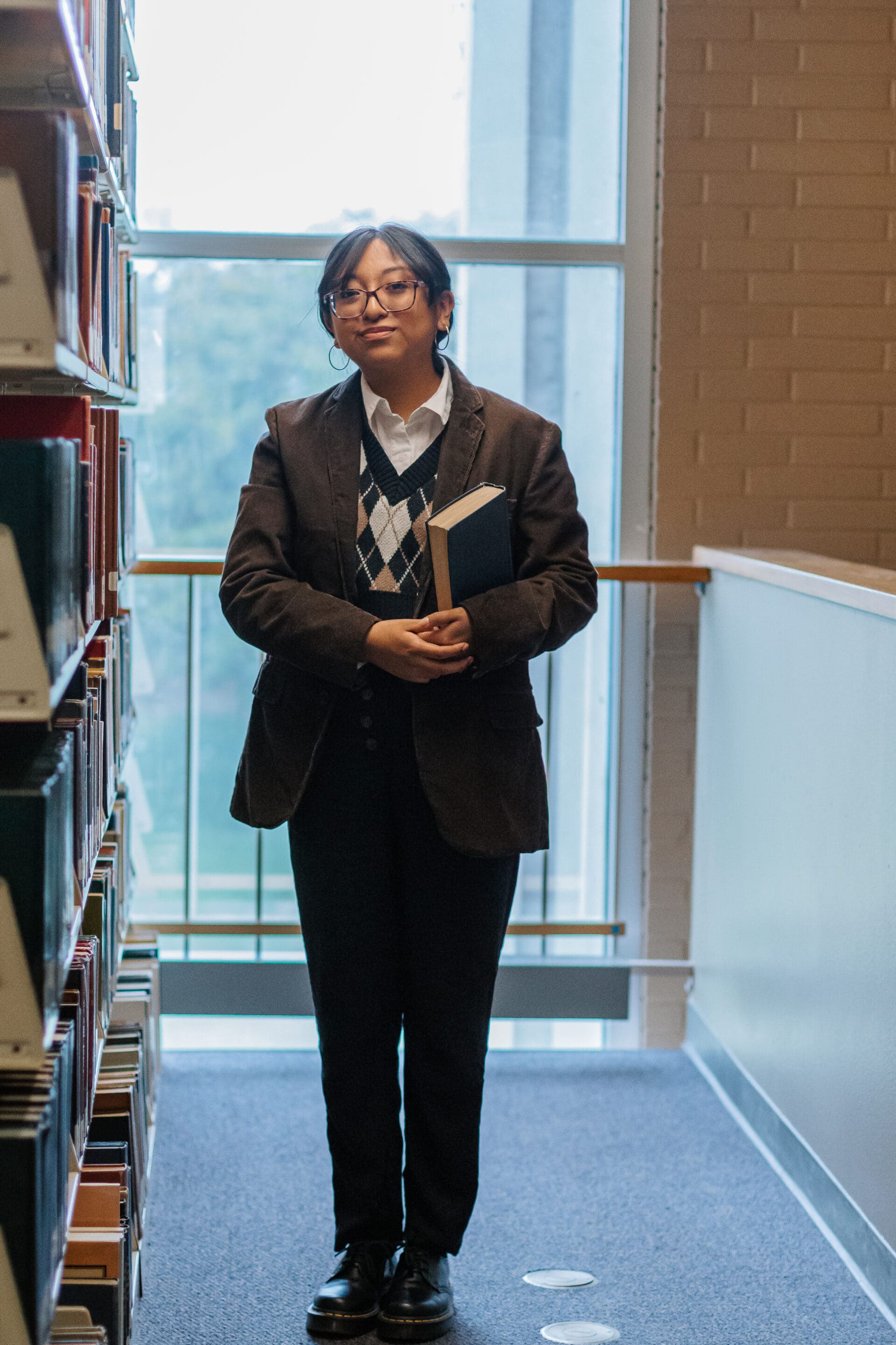 student standing in front of book stack at a library