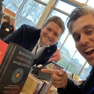 dr felix jager smiling in a selfie with a male friend while pointing at one of his books while its being sold at the conference