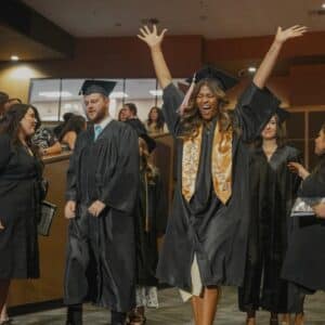 a female student cheering with arms raised while walking into graduation