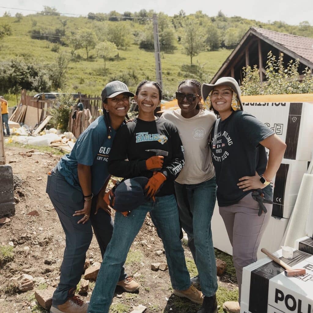 a group of female students smiling together while building a house