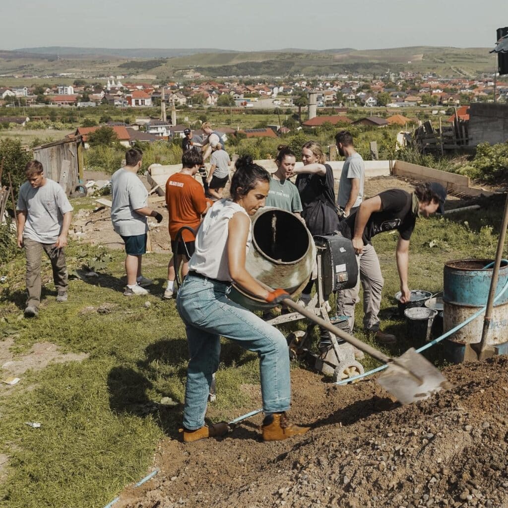 a female student pouring concrete into their house foundation